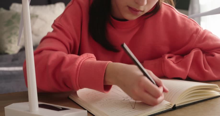 Girl interacting with a wind power model on a table and then writing in a notebook
