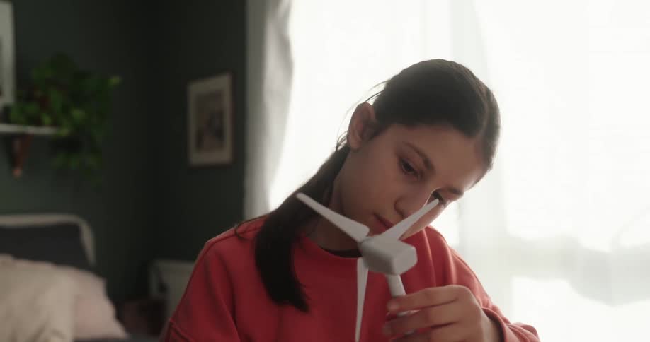 Young girl interacting with wind turbine model while sitting in a room