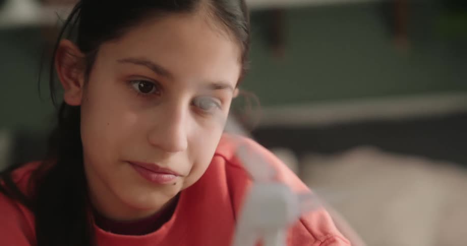 Close up of the face of a girl observing a small windmill model spinning in her room