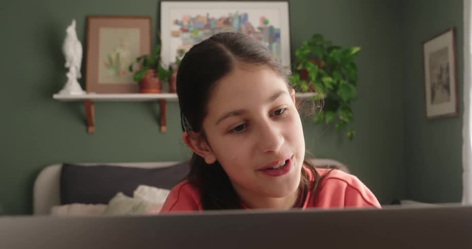 A teenage girl smiles as she talks looking at her laptop