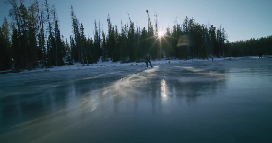 People skating on a frozen lake with conifers in the background