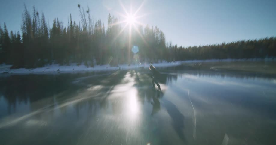 A man holdig a hockey stick is skating in circles on a frozen lake