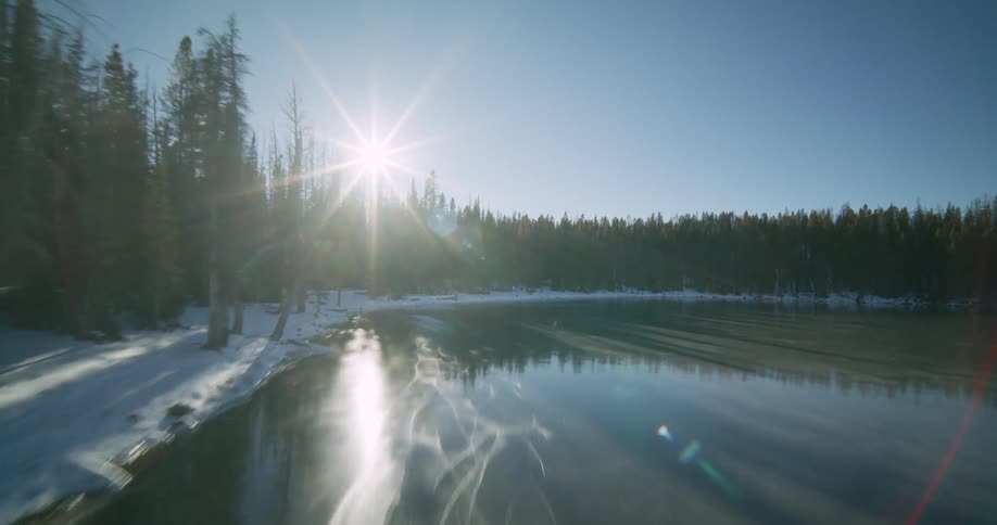 A person ice skates on the frozen lake near the vast forest