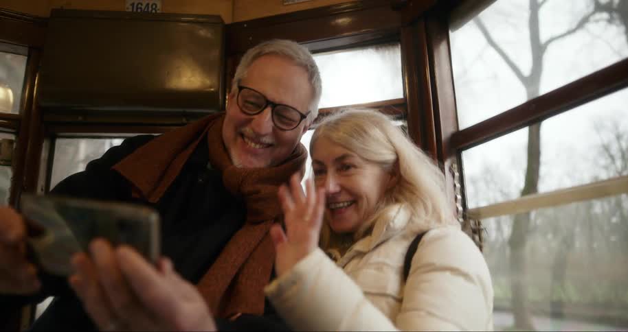 A man and woman talk and wave at a cell phone while riding a trolley train