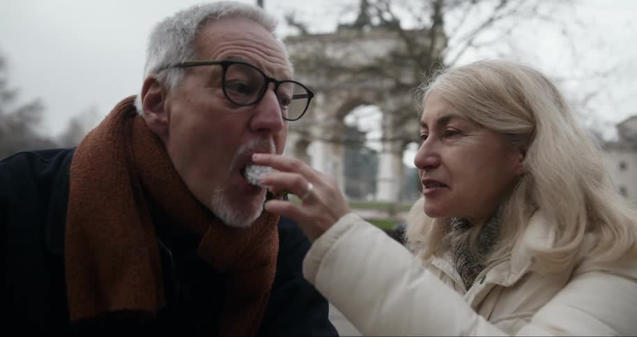 Woman smiles as she feeds a man at an outdoor cafe during a cold day