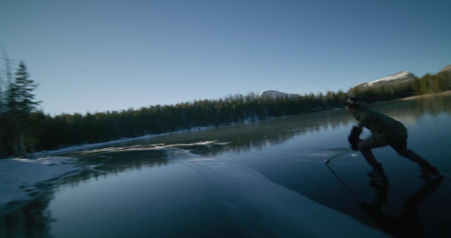 Person skates on a frozen lake surrounded by a pine forest at dusk