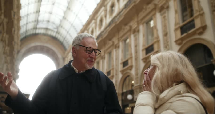 Couple chats animatedly as they walk through a historic gallery with a glass ceiling and classical architecture
