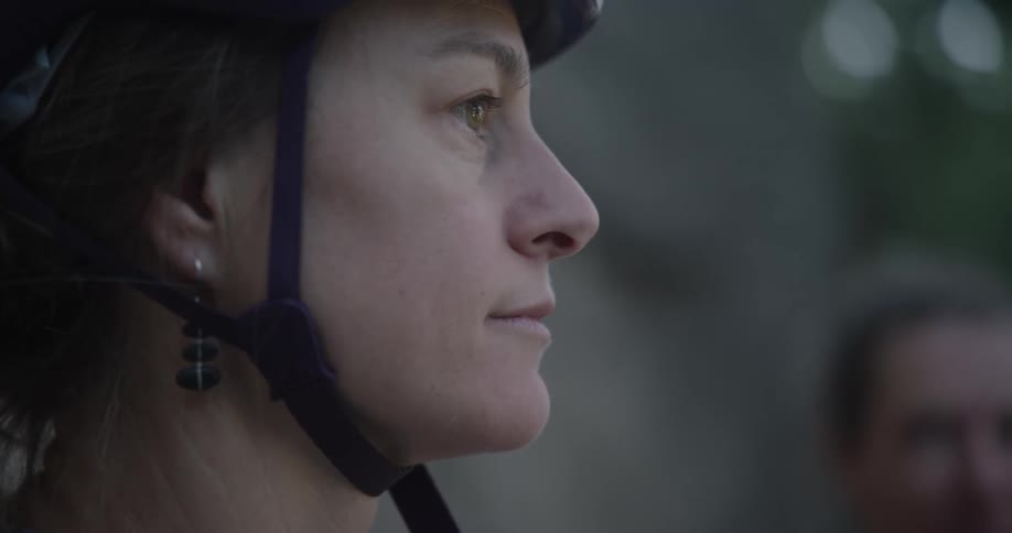 Woman wearing a crash helmet looks down then straight ahead while outdoors