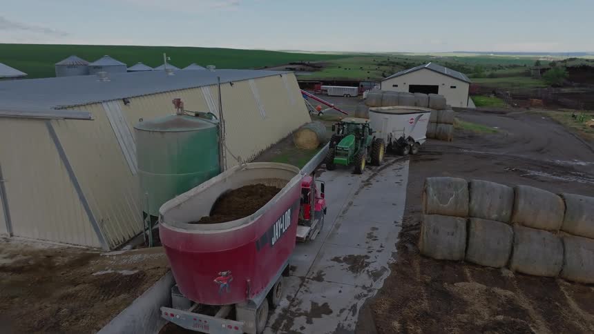 Truck with mixing wagon transports feed on a farm with hay bales around