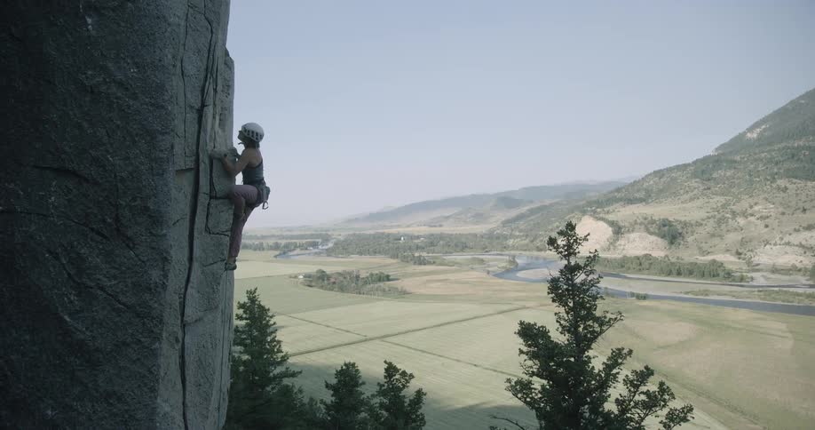 A woman is rock climbing high on a steep mountain