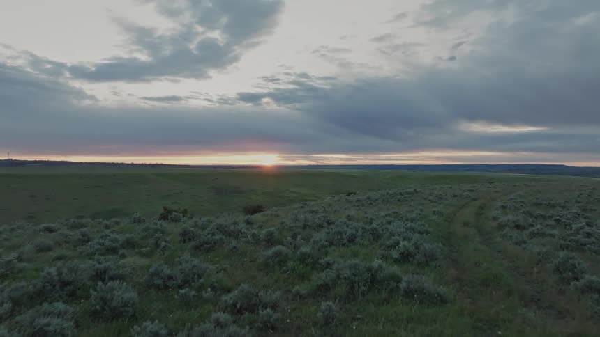 Landscape of open countryside with low vegetation at dusk as the sun sets on the horizon under a cloudy sky