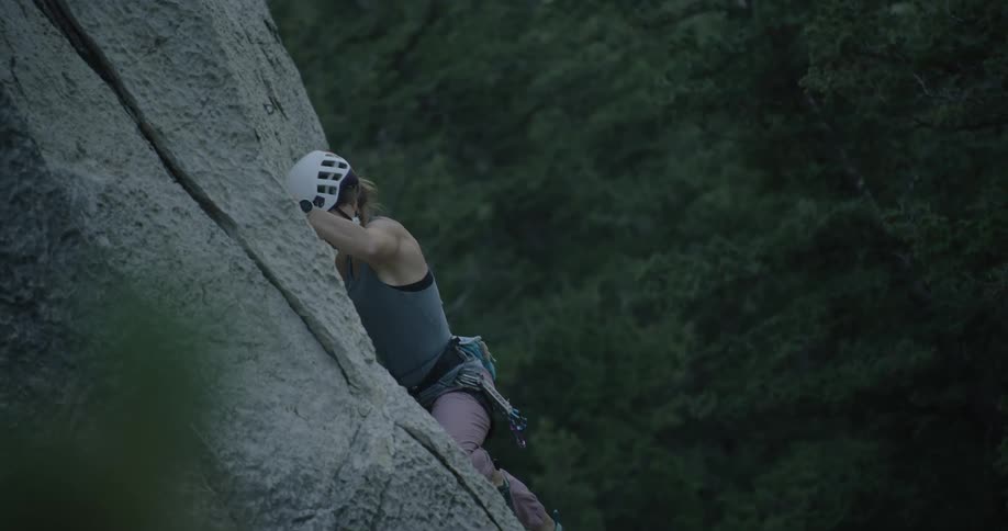 Adventurous woman in helmet climbing a rock wall on a cliff