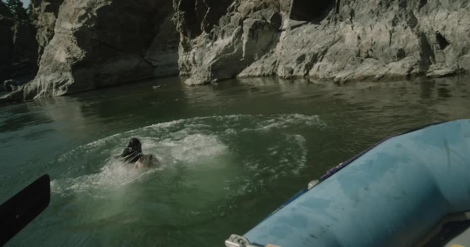 A moment of two people a man and a woman holding hands as they leap off a rocky ledge into the water surrounded by a rugged natural landscape