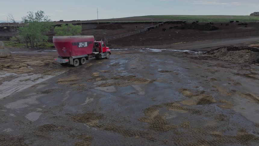 A farm truck moves past bales of hay on a muddy road