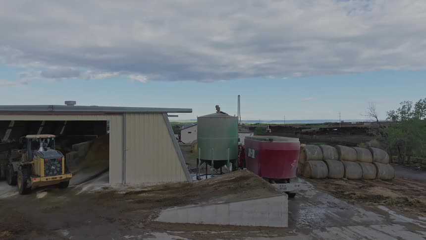 Farm equipment is parked in a shelter near bales of hay