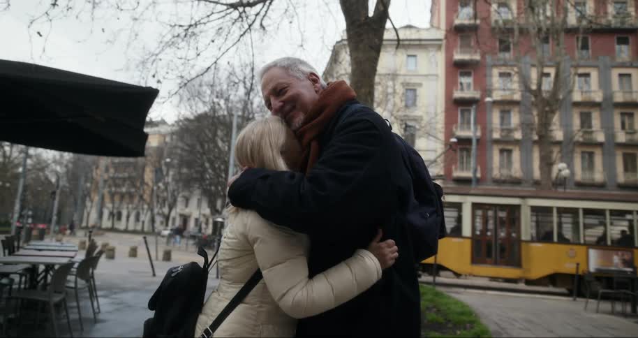An elderly couple hugs on a street in a city