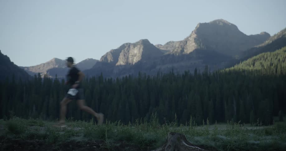 Man with number running on a trail with forests and mountains in the background