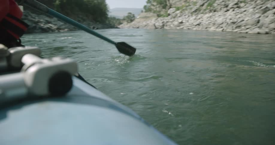 Person riding in a boat rows through the water moving between rock strewn slopes on a cloudy day