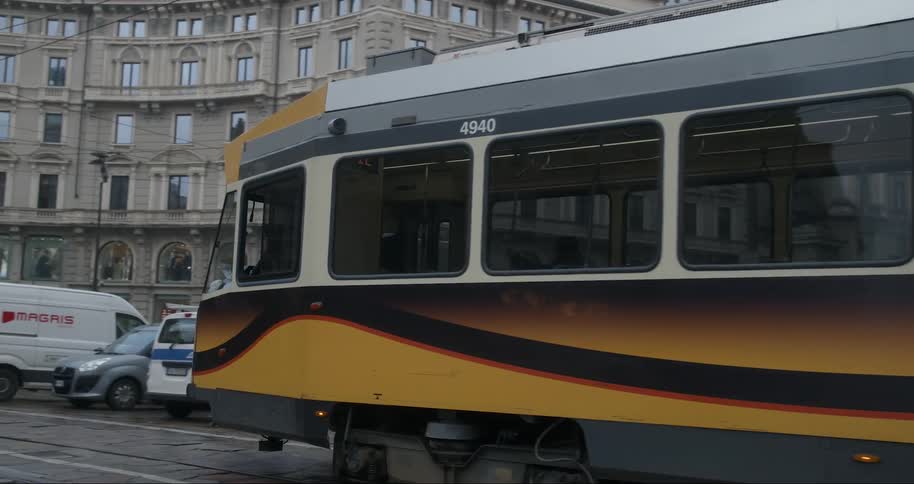 A yellow urban tram driving on the tracks in a city in the middle of the street