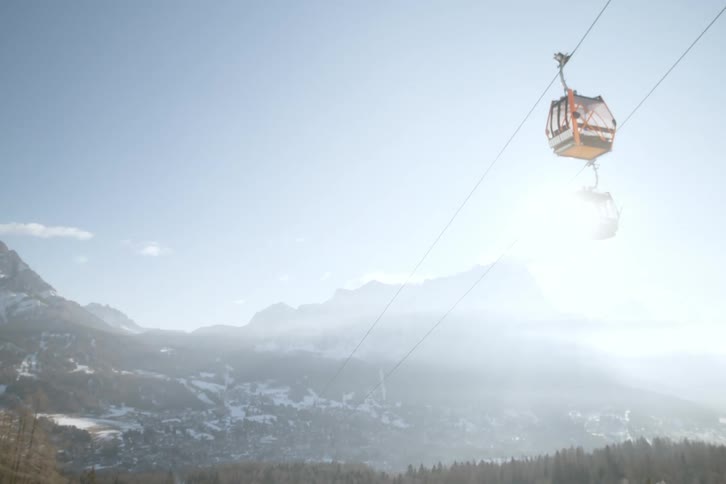 Two cable cars cross paths over a misty mountain landscape under a pale blue sky