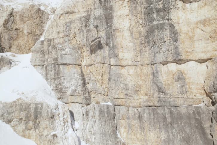 Descending cable car casts a shadow on the cliff near a snow covered mountain slope on a winter day