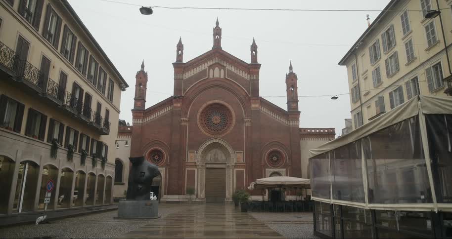 A red brick church santa maria del carmine with a rose window stands at the end of a wet empty cobblestone street lined with buildings under a gray sky