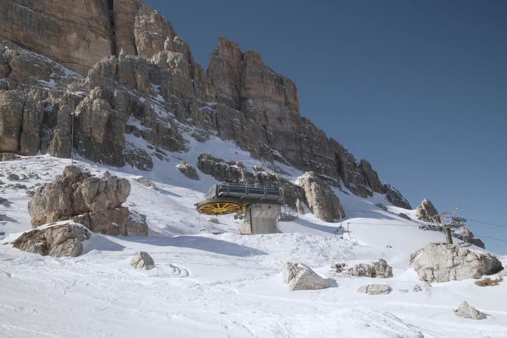 A large yellow pulley turning the cables of a cable car on a snowcovered mountain