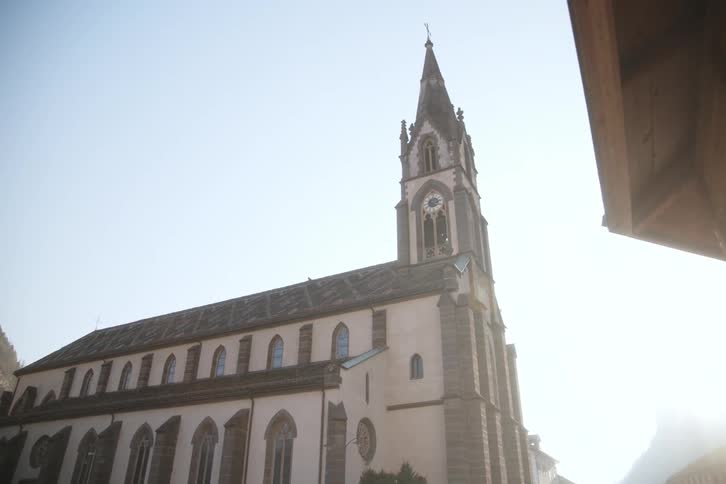 A church with a large pointed tower on a day with clear skies and sun flares