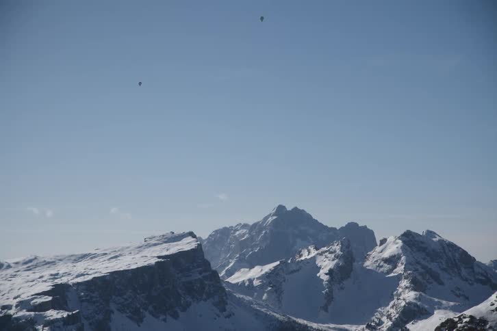 Two people are parachuting on a clear day above a snowcovered mountain range