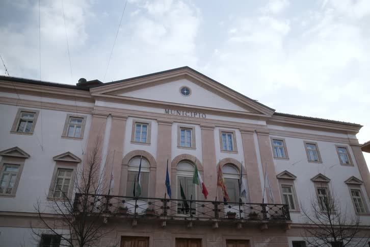 Facade of a classic municipal building with flags flying from the balcony and a partly cloudy sky in the background