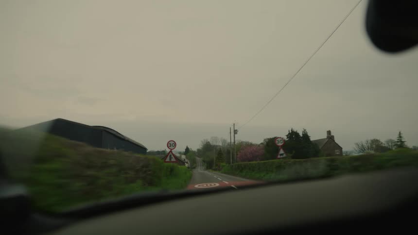 Interior view of the windshield of a vehicle moving along a paved road in a rural area