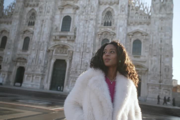 A woman in a white fur coat stands in front of the duomo di milano