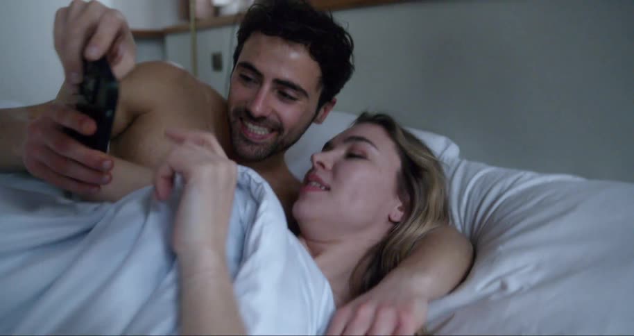 A couple look at their cell phone in bed