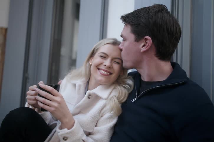 A young couple sits outdoors cuddling and sitting closely together