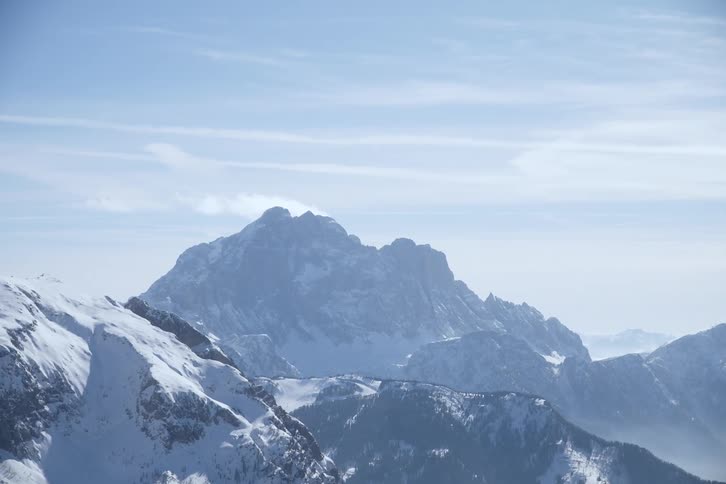 A wide shot captures snow covered mountains under a hazy blue sky