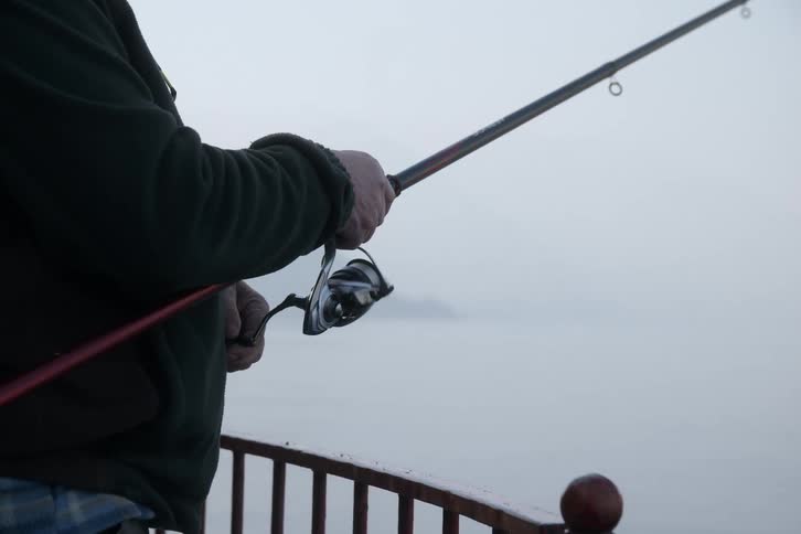 A persons hand using a fishing rod and turning the pulley to pull the line
