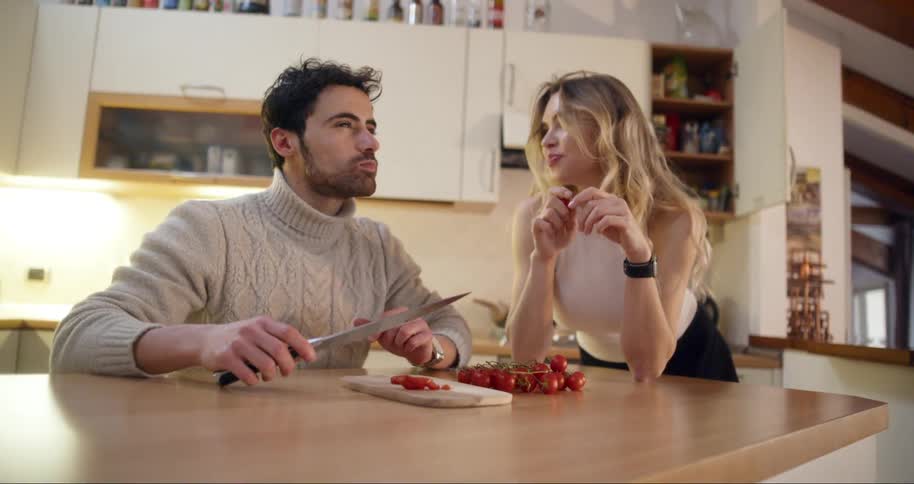Woman and a man in the kitchen on a wooden countertop eating tomatoes