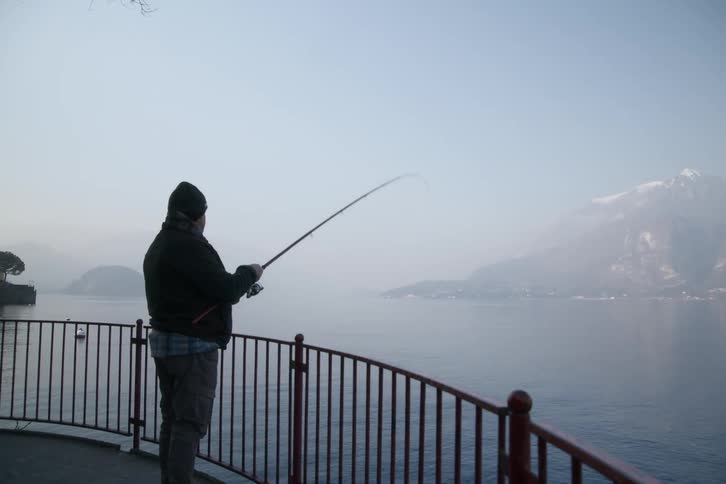 A person is standing using a fishing rod to fish in a large body of water