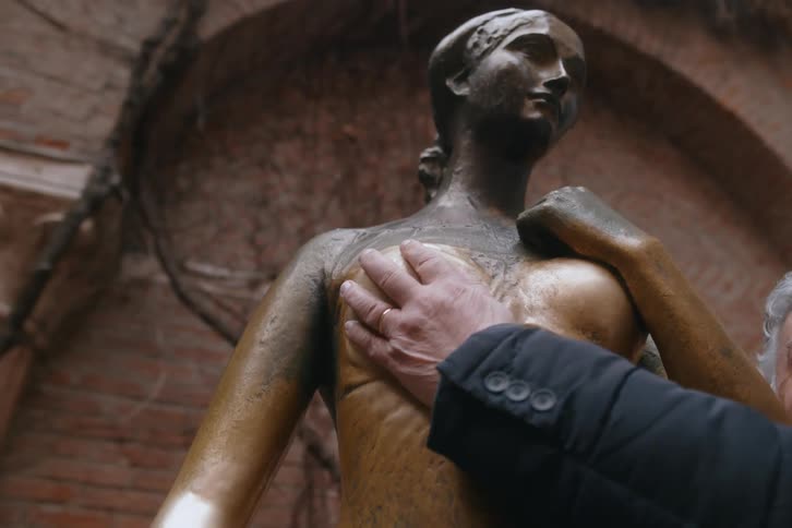 Persons hand on the chest of a bronze statue of a woman