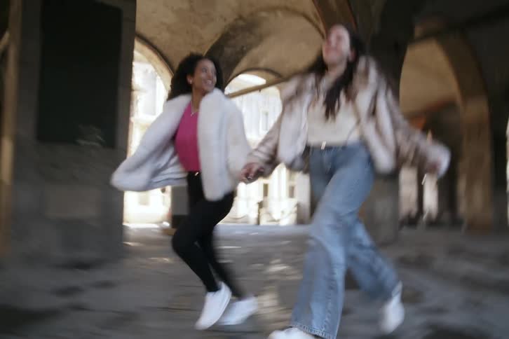 Two happy friends holding hands running down the street together