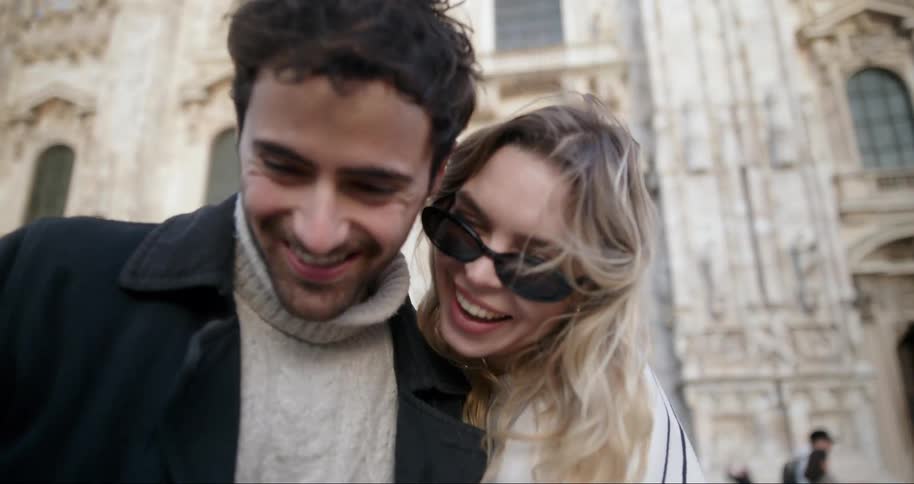A smiling couple takes a selfie in front of an ornate building