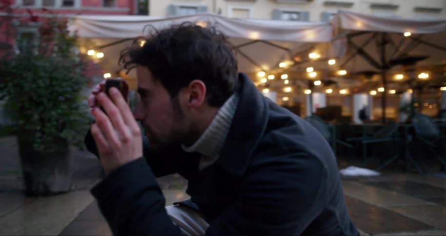 A man is photographing a woman posing in front of a building