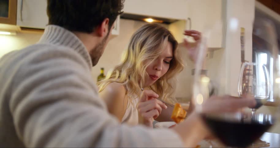 A couple eats a pasta dish with glasses of red wine at a kitchen table