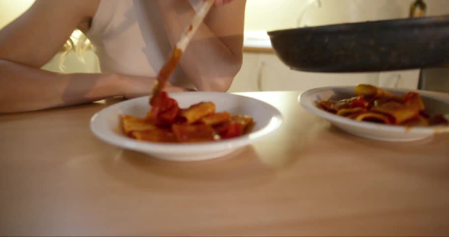 Hands with a spatula serving pasta in tomato sauce to a smiling seated woman