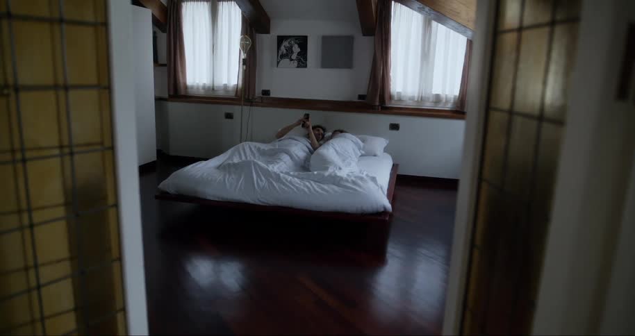 A young couple wakes up on a bed in a tidy bedroom at home in the morning