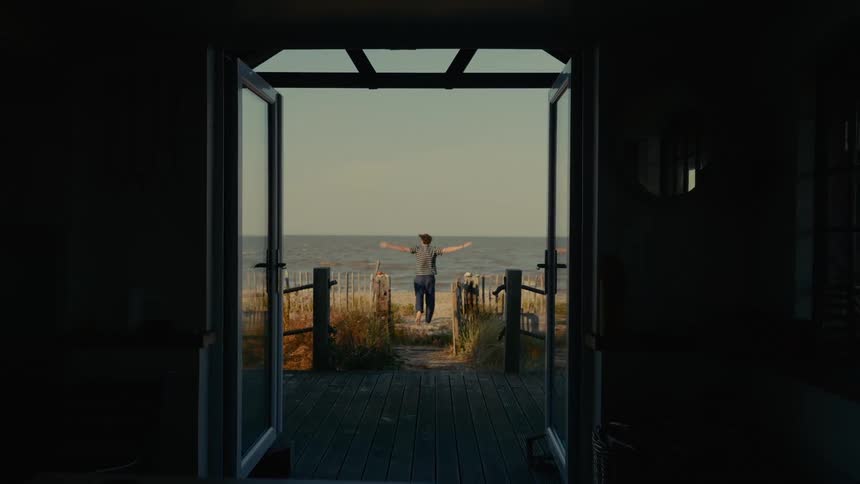 View of an open door to a beach and a person with open arms