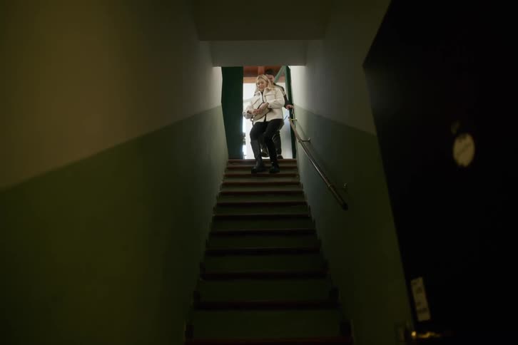 A woman and man hurry down a narrow staircase in a building