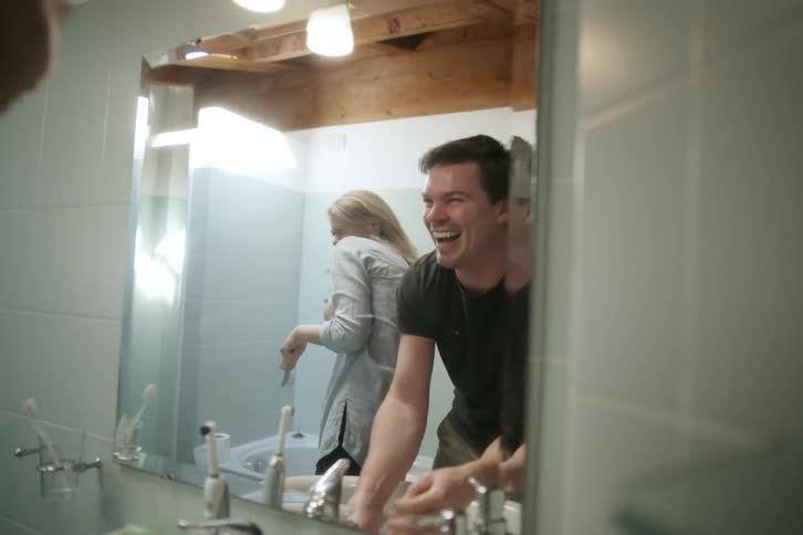 Woman and a man standing in front of the mirror together in the bathroom laughing