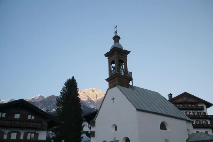 Church with a small bell tower surrounded by townhouses and snowy mountains on the horizon