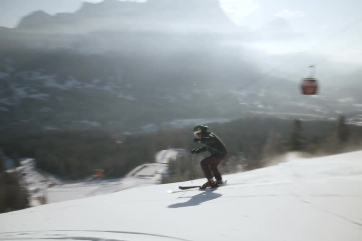 A person skiing on a hill that is covered in snow and does a maneuver to the side that throws a lot of snow